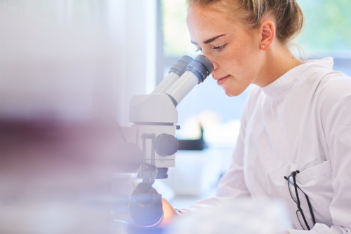 A woman scientist in a lab coat looks through a microscope