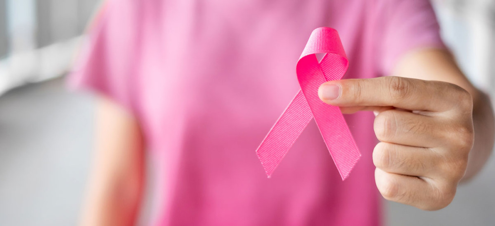 A person in a pink shirt holds a pink ribbon to the camera