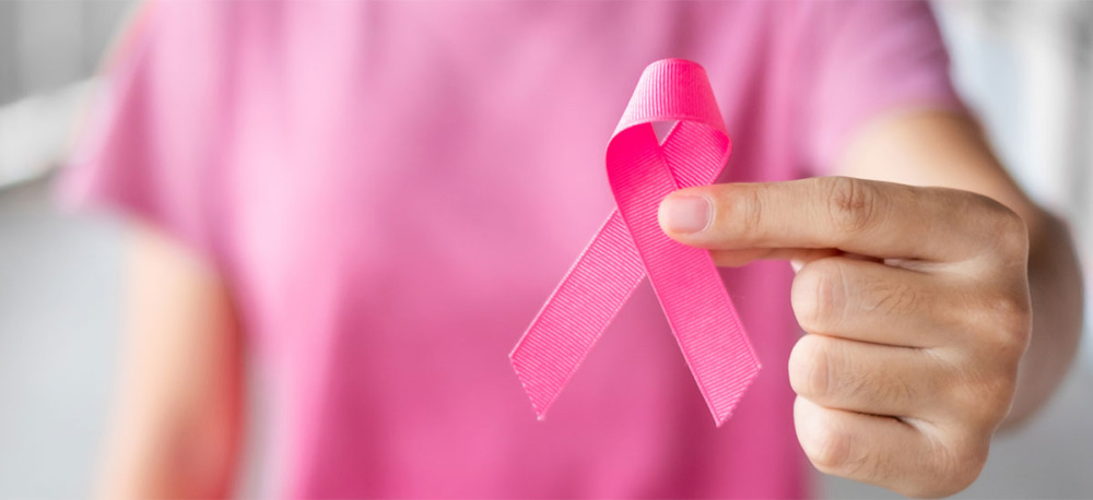 A person in a pink shirt holds a pink ribbon up to the camera