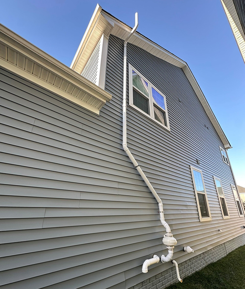 A radon mitigation system on the side of a gray house.