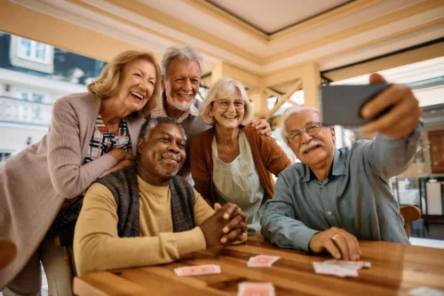 Multiracial group of happy senior people taking a selfie with a cell phone in a recreational room.