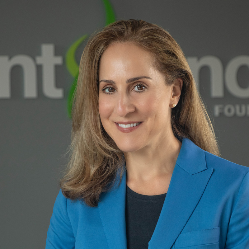 Headshot of Prevent Cancer Foundation CEO, Jody Hoyos. She has medium-long brown hair, brown eyes and is smiling. She is wearing a bright blue blazer over a black shirt and pearl earrings.