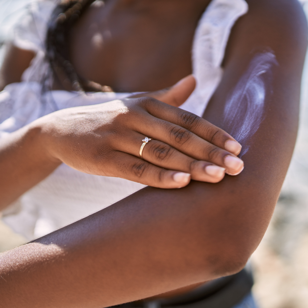 A Black woman applies sunscreen on her arm.