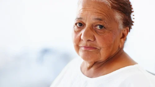 A closeup portrait of a senior woman who is looking hopeful at the camera.