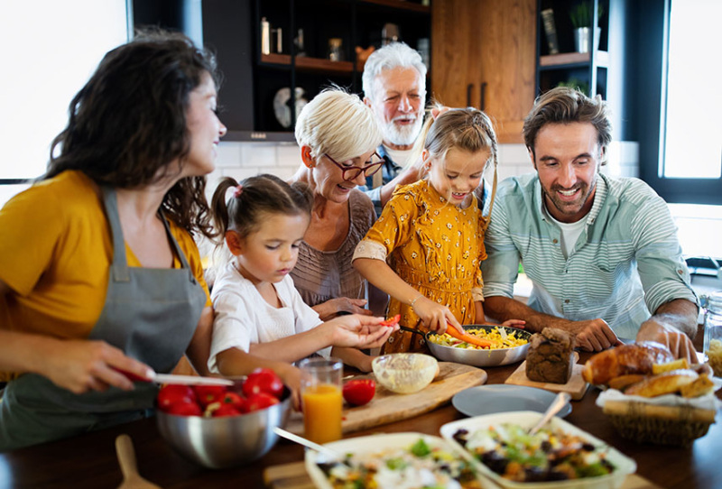 A multi-generational family gathers in a brightly lit kitchen to prepare breast fast.