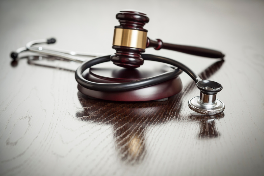 A gavel and a stethoscope are intertwined on a wooden surface.