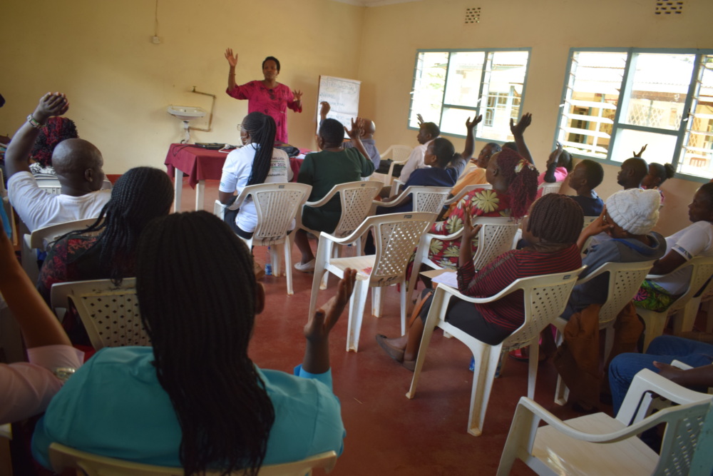 A woman at the front of a room trains a group of seated community health workers in Kenya.
