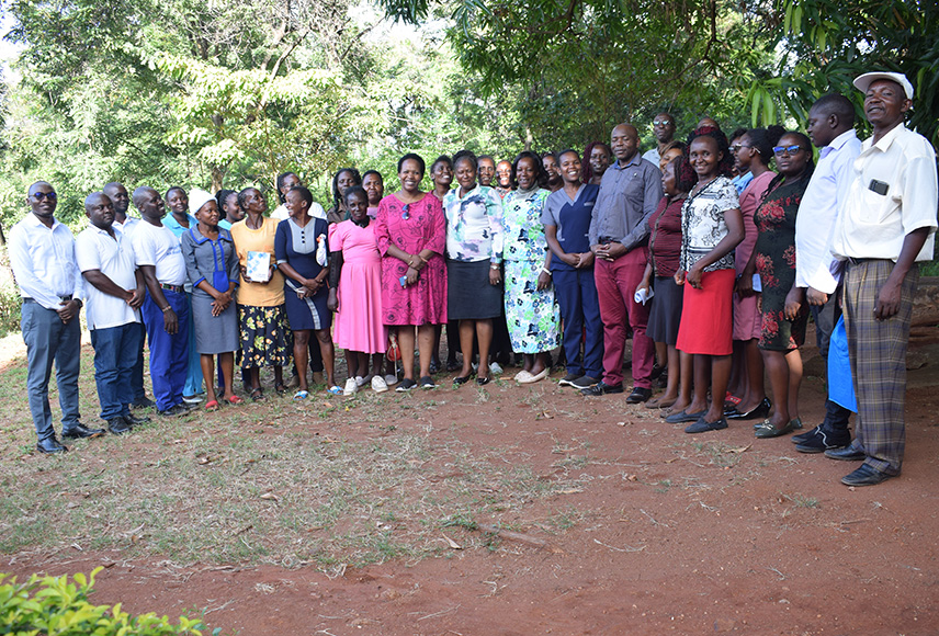 A group of adults pose outside after completing a CPH training in Kenya. There are both men and women dressed in business casual clothing and they are smiling toward the camera.