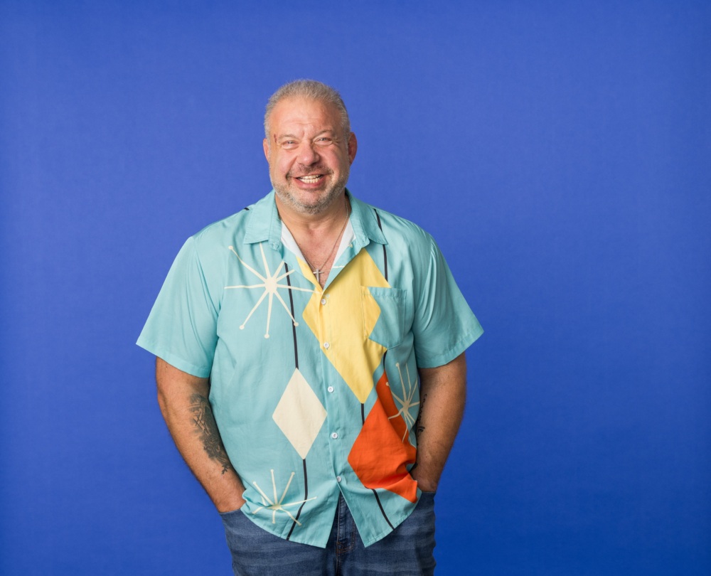 Author Michael Holtz stands with his hands in his pockets, wearing a light blue bowling shirt and blue jeans.