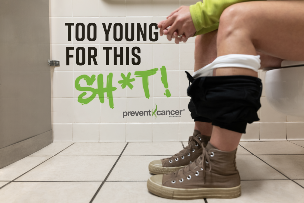 A woman is seated on a toilet in a restroom stall. You can only see her legs and her pants are pulled down around her ankles. She is wearing hightop sneakers. There is "graffiti" on the tiled wall next her that reads, "Too Young for This Sh*t!"