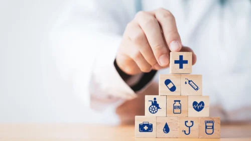 A health care professional stacks toy wooden blocks, with each block showing an image of a different medical object.