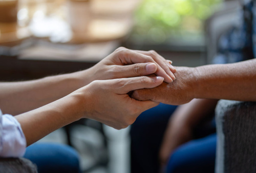 A close up image of hands. The hands on the left are clasping one hand of the other person as it to comfort them.