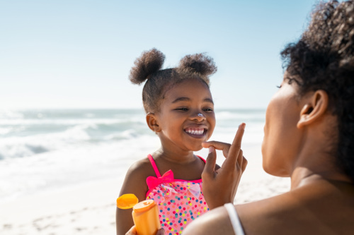 A woman dots sunscreen on a little girl's nose at the beach.