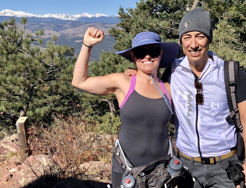 A woman flexes her arm while hiking outdoors with her husband.