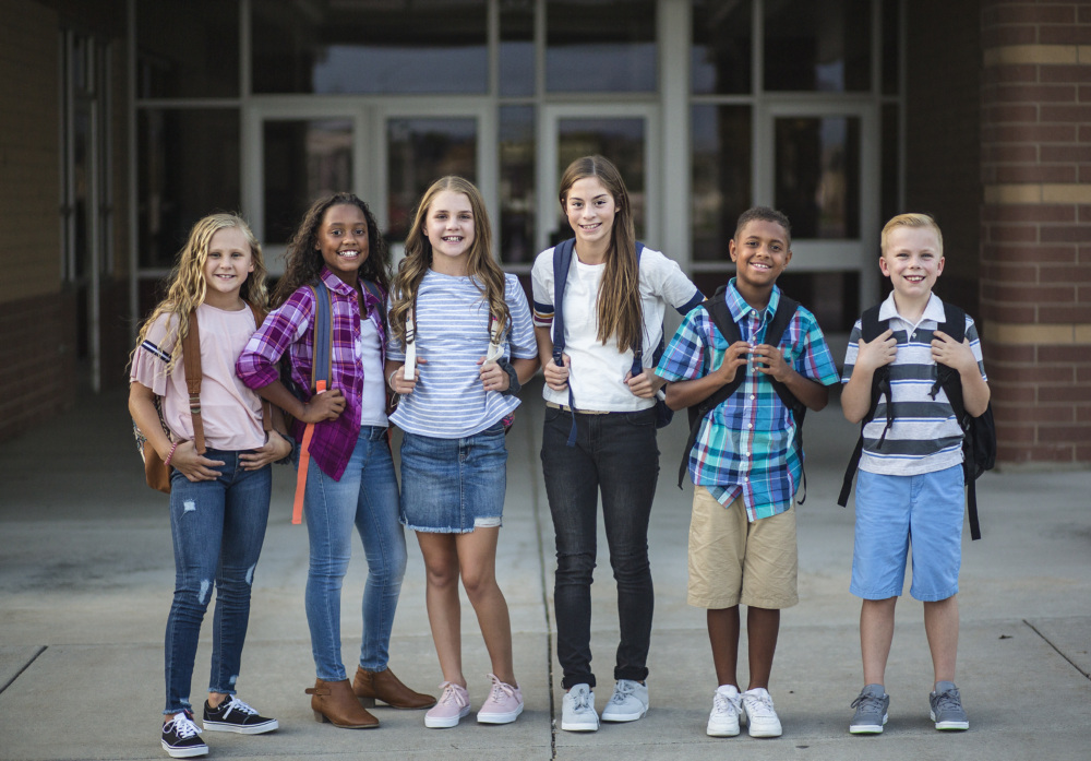 A group of boys and girls with backpacks standing in front of a school.