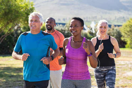 Four middle aged people in workout clothes power walk outside