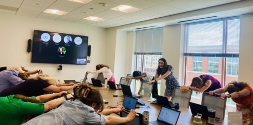 The Prevent Cancer Foundation staff reach their arms onto chairs and stretch in the conference room.