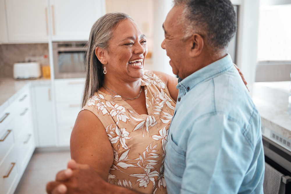 A man and woman in their 70s dance in the kitchen