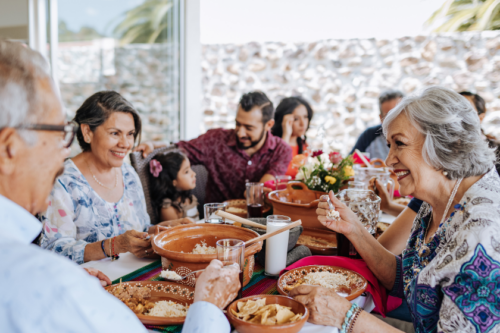 A Hispanic family sits around a table outside, eating a meal together