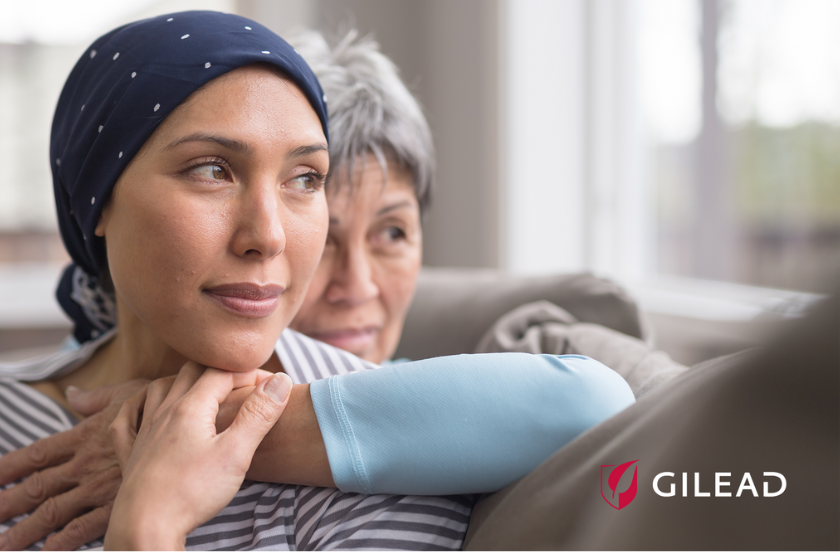 A woman in a headscarf sits with an older woman embracing her from behind. A Gilead Sciences logo is in the bottom right corner.