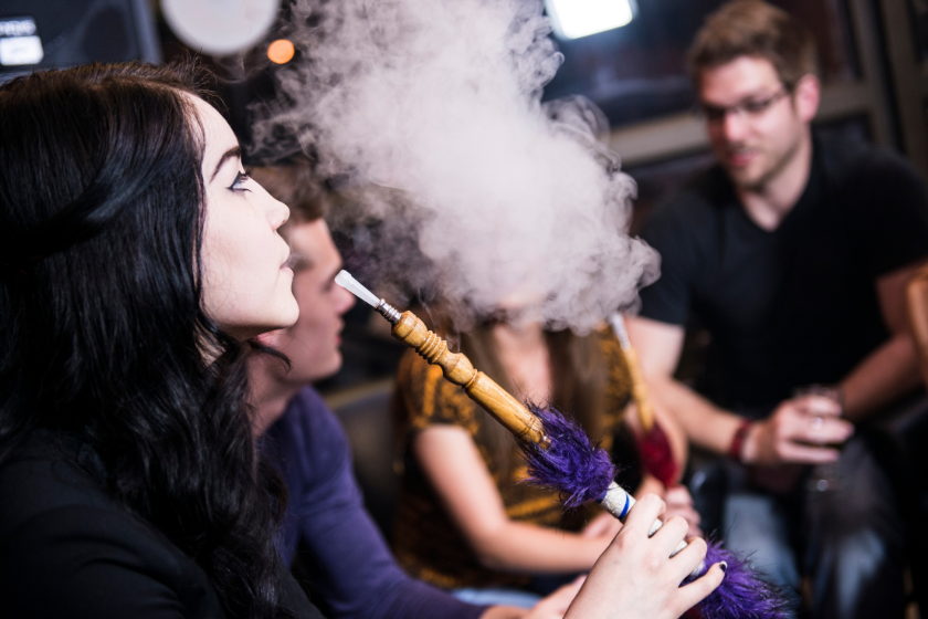 A group of young adults smoke hookah in a bar