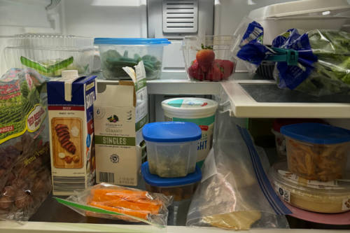 A refrigerator shelf with carrots, strawberries, beef broth, hummus, grapes, green beans and more