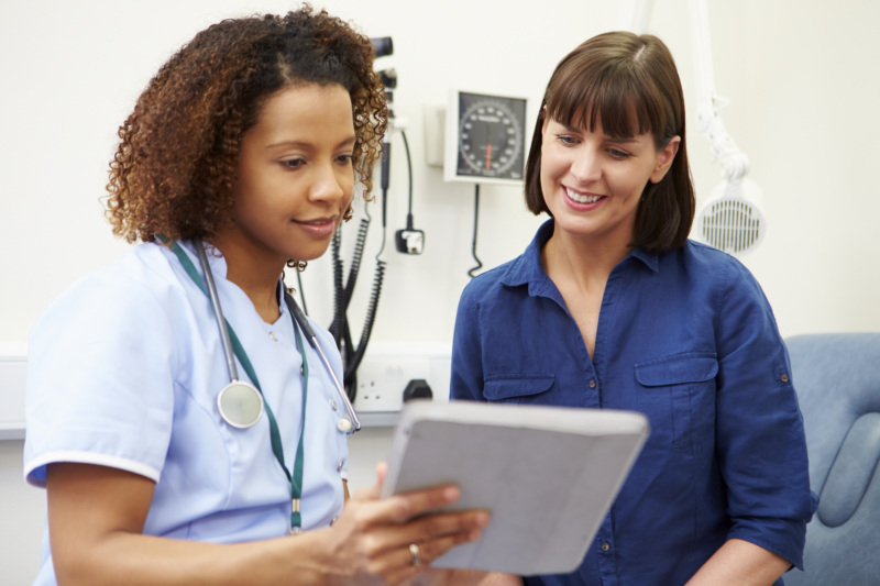 In a doctor's office, a nurse shows a smiling woman a tablet.