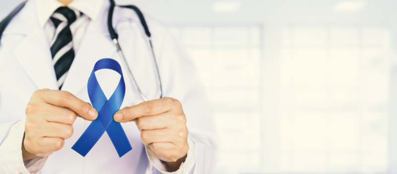 A doctor holds a blue ribbon to represent colorectal cancer awareness