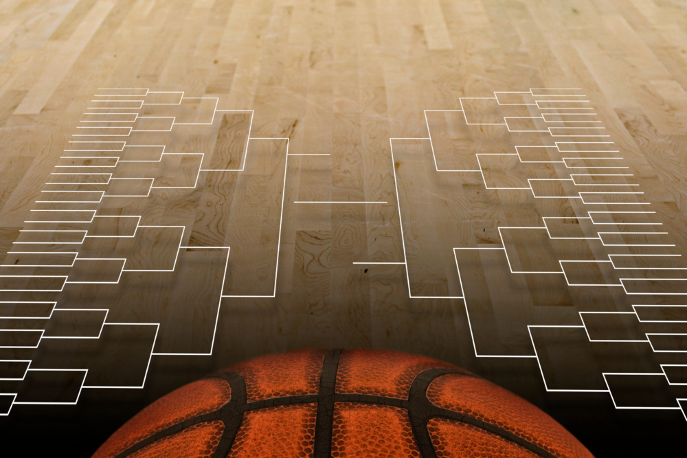 A March Madness college basketball bracket is displayed against a wooden court backdrop, with a large orange basketball in the foreground.