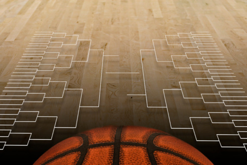 A March Madness college basketball bracket is displayed against a wooden court backdrop, with a large orange basketball in the foreground.