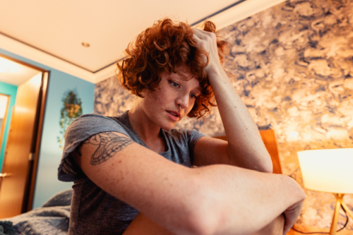 A woman sits in her bedroom with an anxious expression