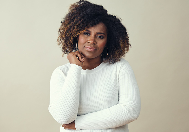 3/4 portrait of a Black woman in her 30s facing the camera. She has a somber but hopeful expression on her face.