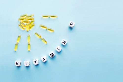 Yellow pills form a sun shape. Plastic beads spell out “Vitamin D.”