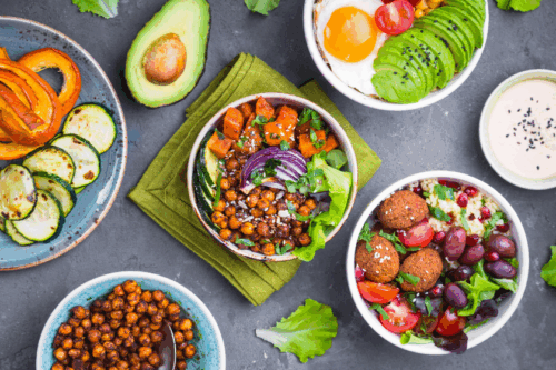 An aerial photo of salad bowls with a mix of different ingredients, including falafel, olives, roasted chickpeas, an egg, avocado, roasted squash and zucchini.