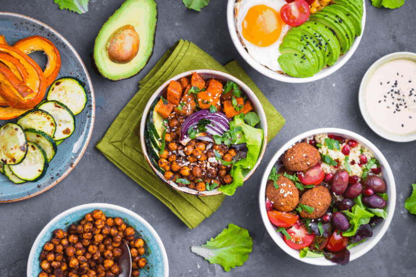 An aerial photo of salad bowls with a mix of different ingredients, including falafel, olives, roasted chickpeas, an egg, avocado, roasted squash and zucchini.