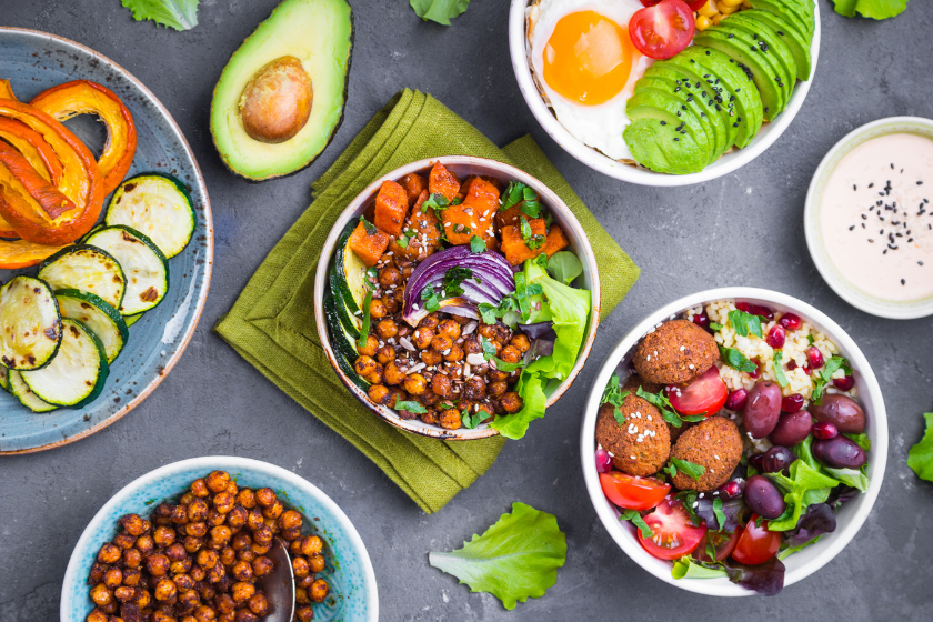 An aerial photo of salad bowls with a mix of different ingredients, including falafel, olives, roasted chickpeas, an egg, avocado, roasted squash and zucchini.
