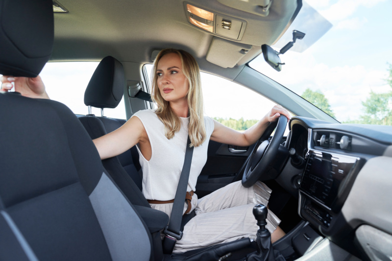 A woman in the drivers seat looks back over her shoulder as she backs her vehicle up.