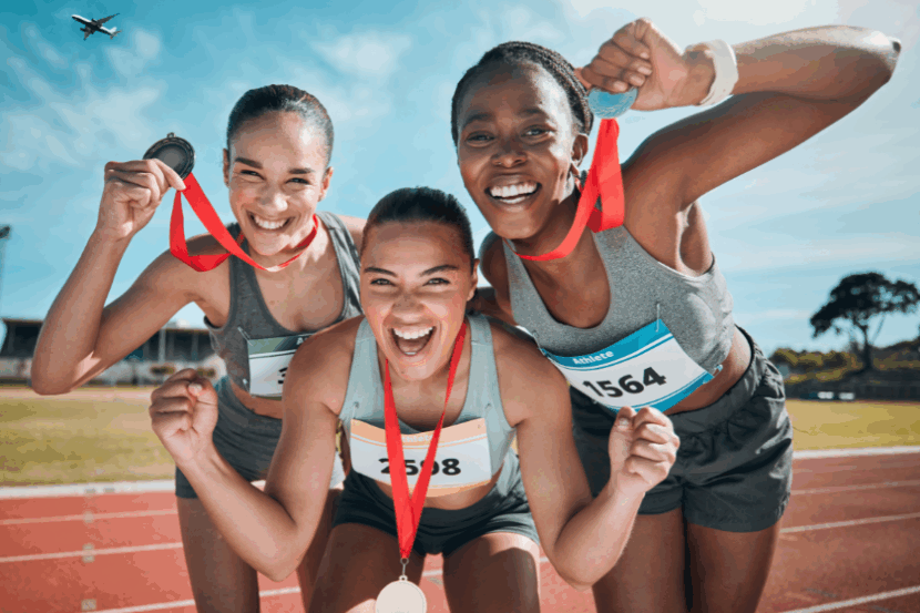Three teenaged girls hold up metals outside on a track.