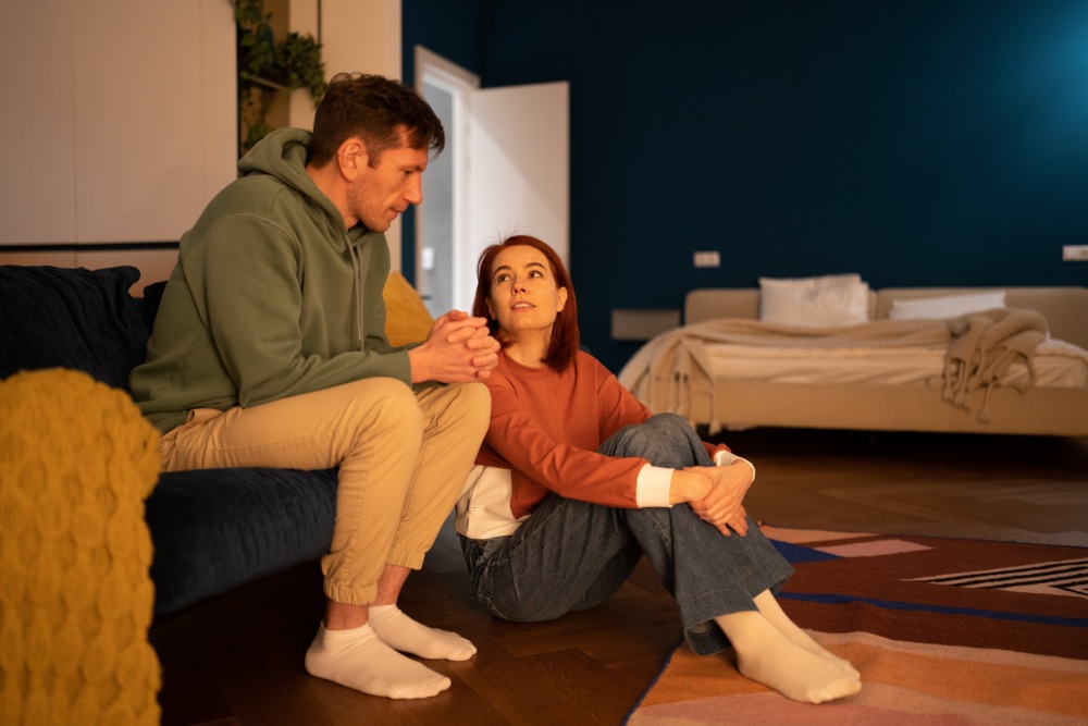 A couple, male and female, sit on a couch having a serious conversation.