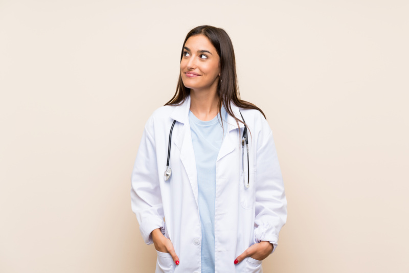Young female doctor looks up in front of beige background.