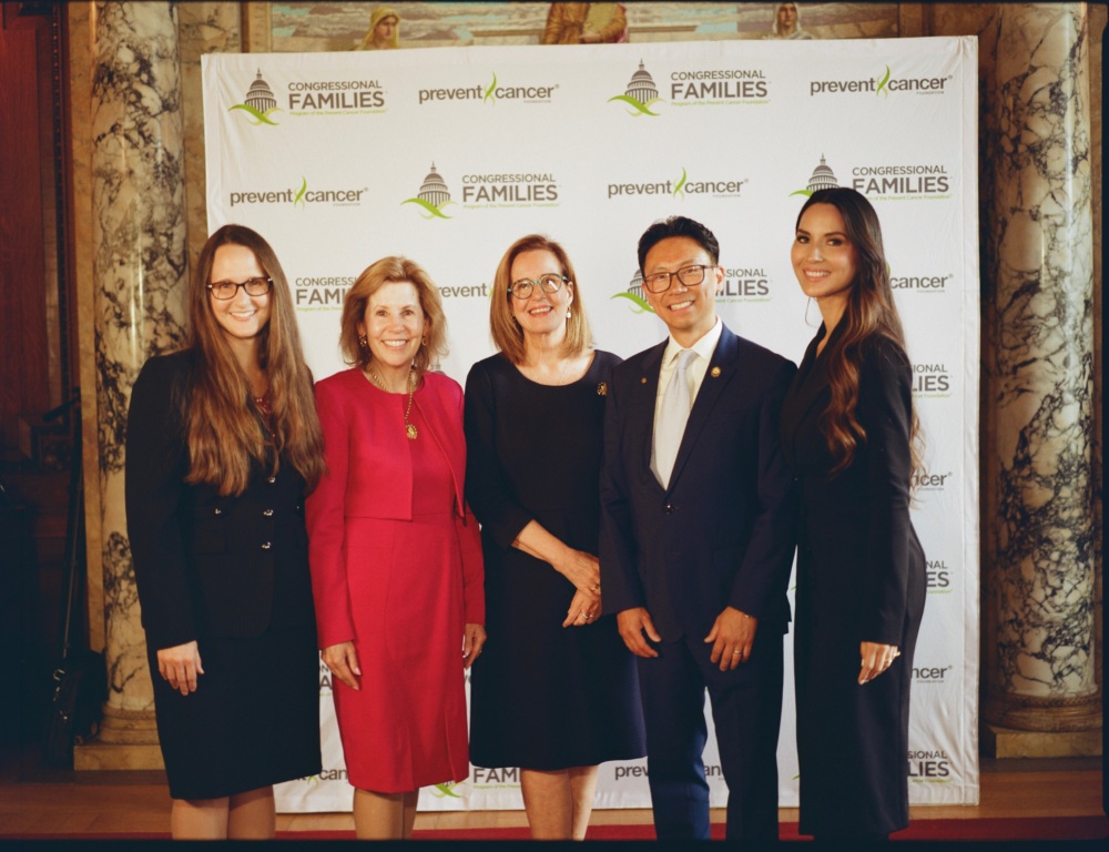 Five people dressed professionally stand in front of a backdrop as they pose for a photo.