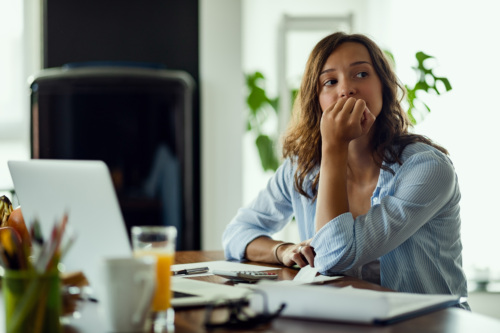 A woman sits at a desk with her hand on her mouth, with a look of concern on her face.