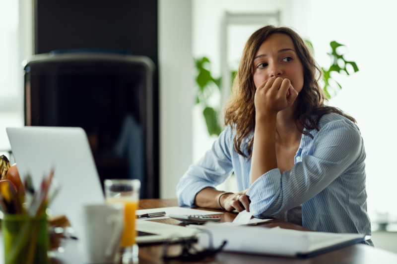 A woman sits at a desk with her hand on her mouth, with a look of concern on her face.