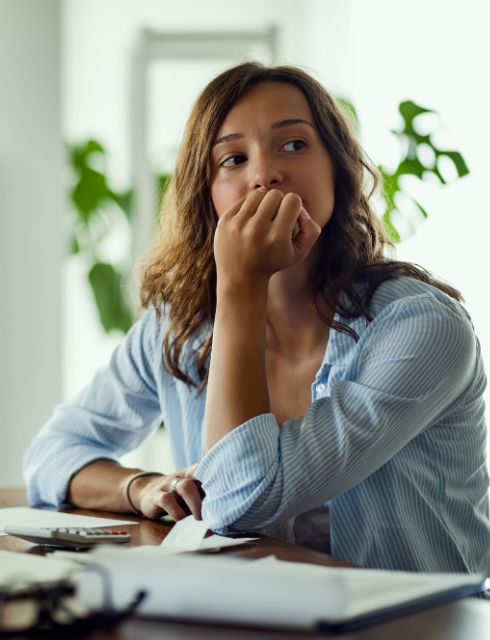 A woman sits at a desk with her hand on her mouth, with a look of concern on her face.