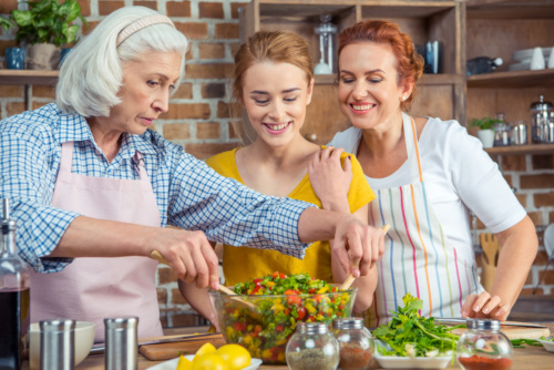 Grandma, mother and daughter tossing a salad in the kitchen together.