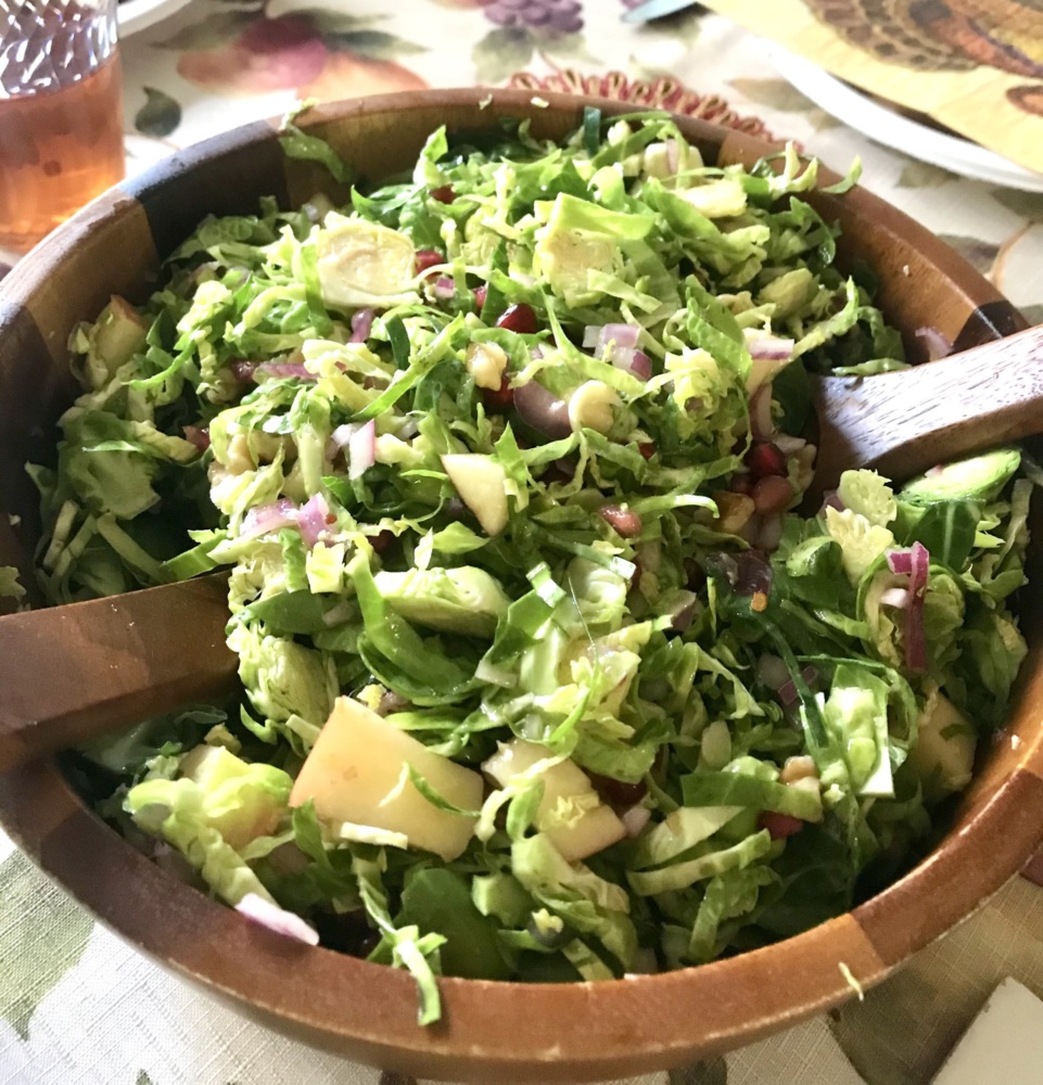 An image of a brussels sprouts salad in a wooden bowl on a table set for Thanksgiving.