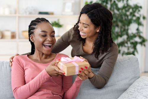 Woman giving a present to a happy friend in pink shirt.