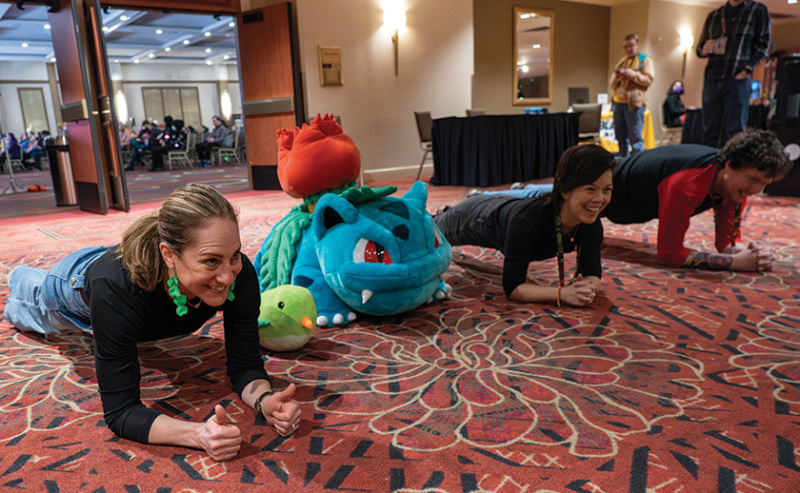 Three people are doing planks next to a giant plush Pokemon