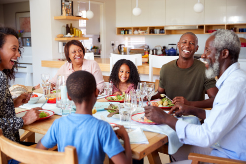 Family sitting down at dinner table together laughing and smiling.