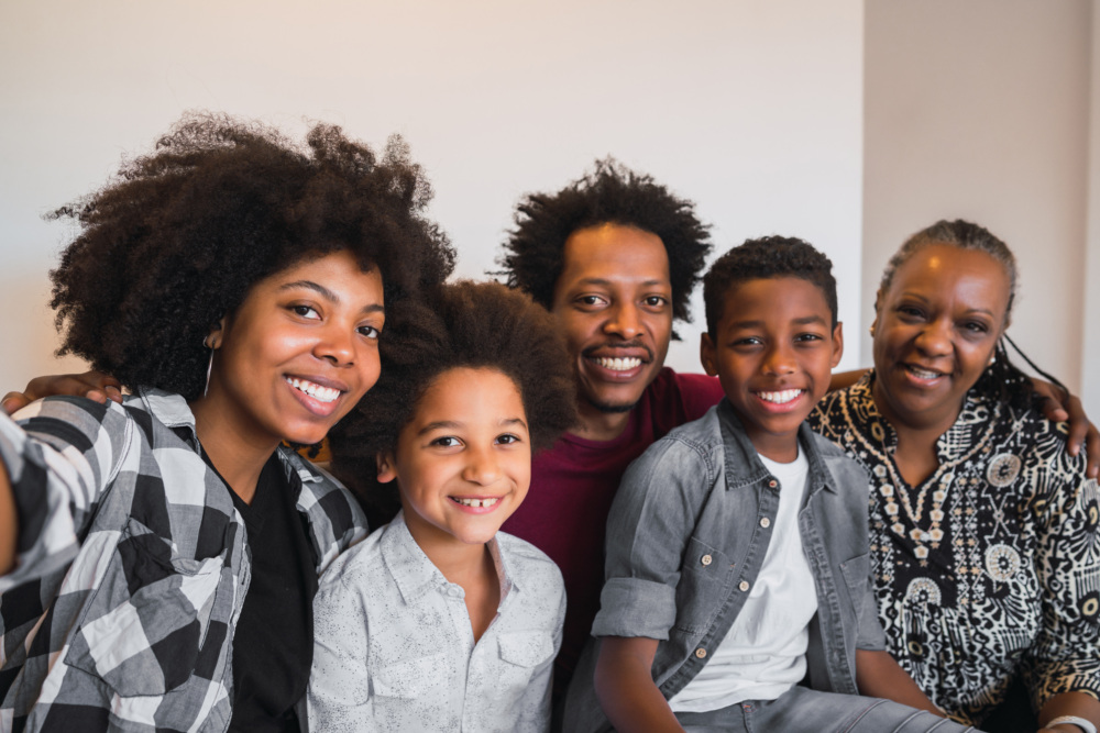 A Black family consisting of three adults and two children take a selfie, smiling.